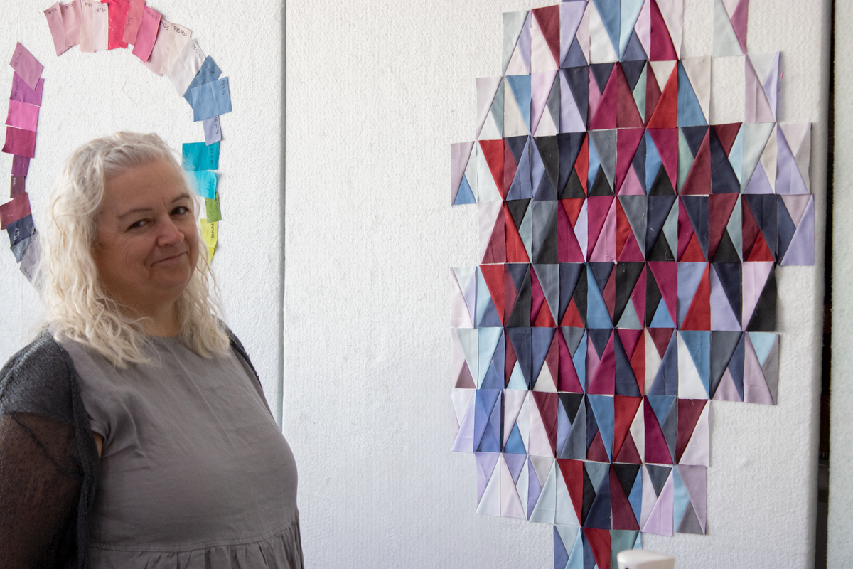 Quilt retreat participant in gray top, standing beside red white blue quilt block display