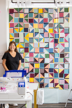 Quilt retreat sewing room with participant standing by white sewing machine and quilt wall
