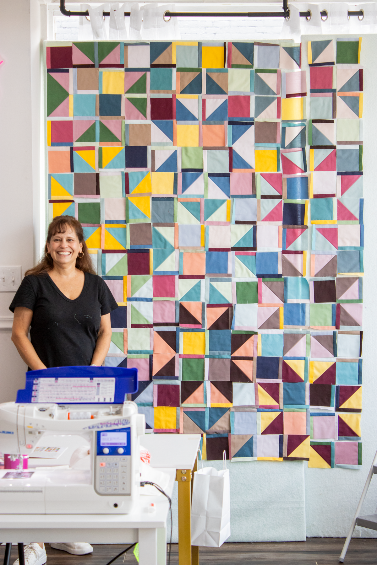 Quilt retreat sewing room with participant standing by white sewing machine and quilt wall