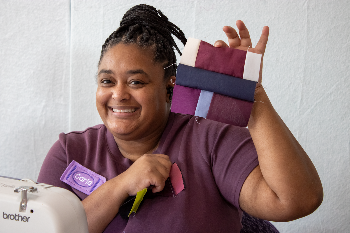 Quilt retreat participant smiling, holding folded fabric blocks near Brother sewing machine