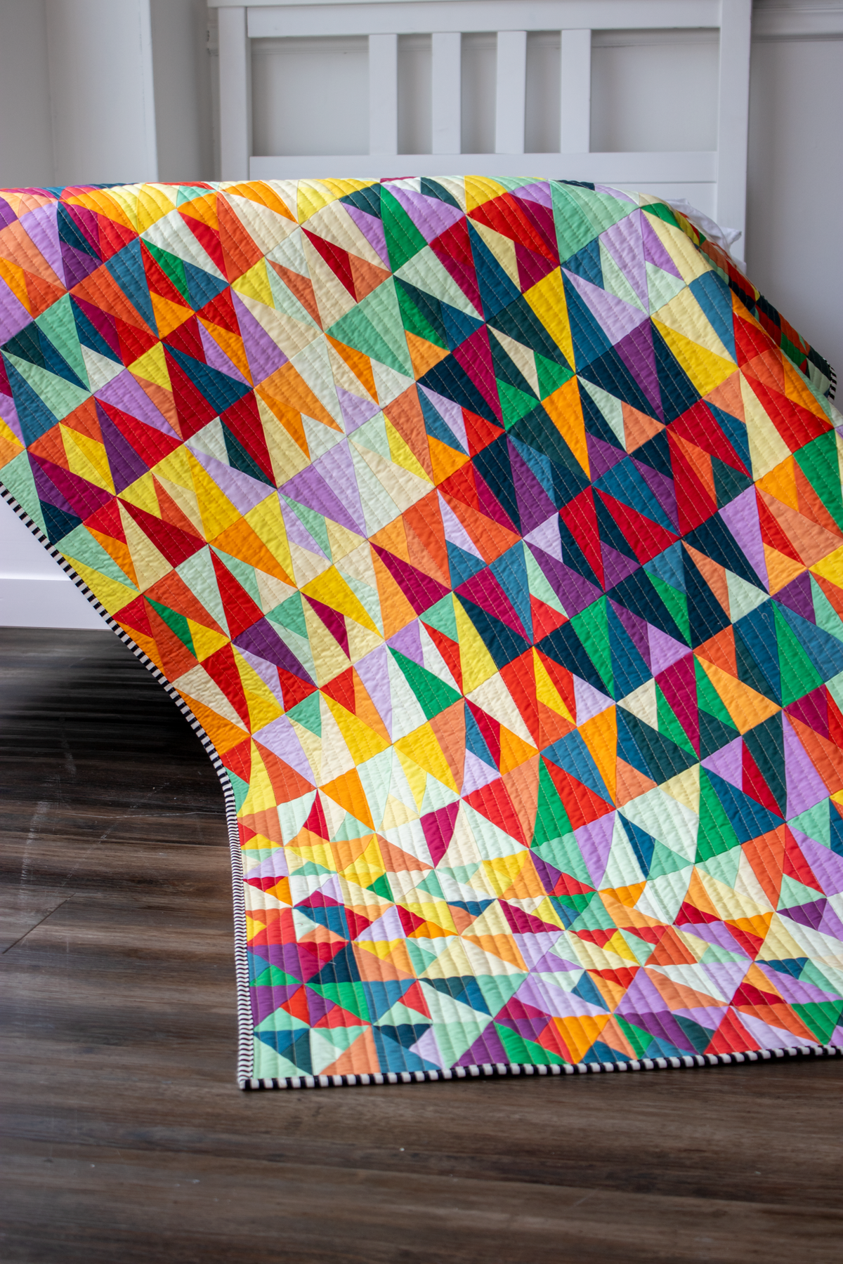 Multicolor geometric triangle quilt draped over bed, showing stitched patchwork